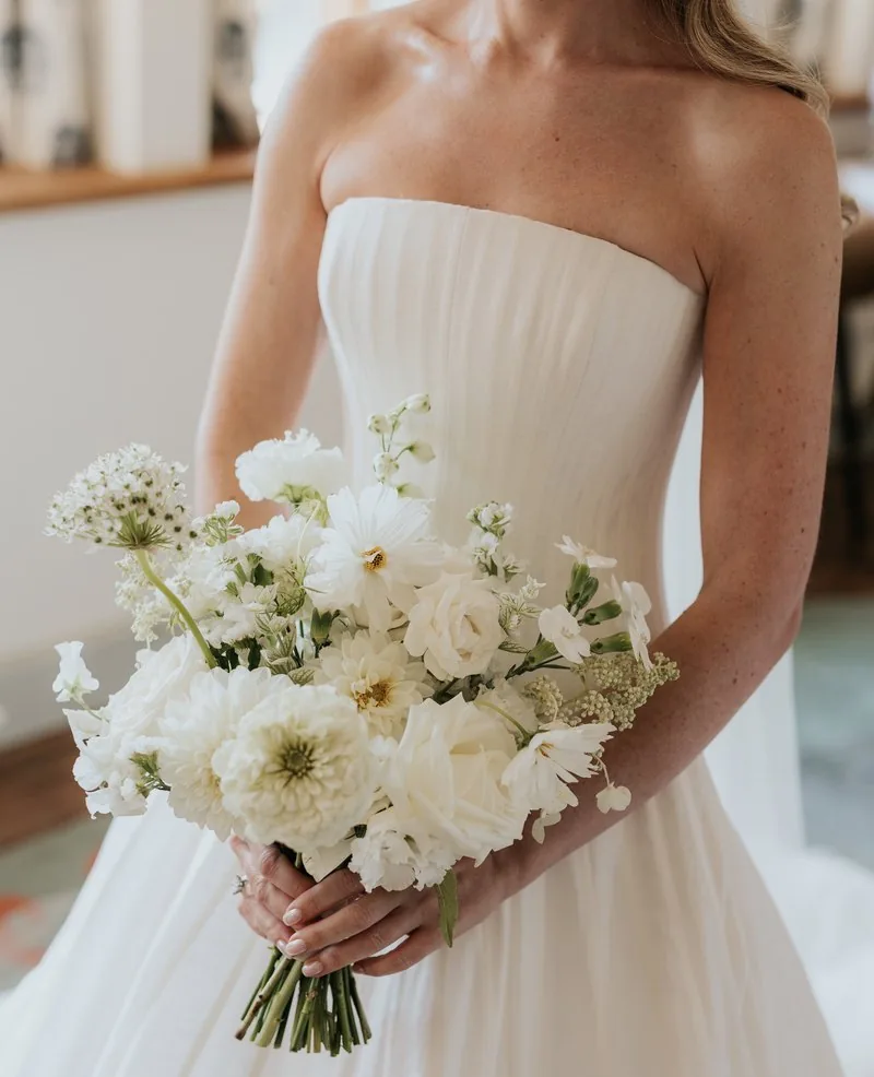 A bride holding a white bouquet of white roses and dahlias